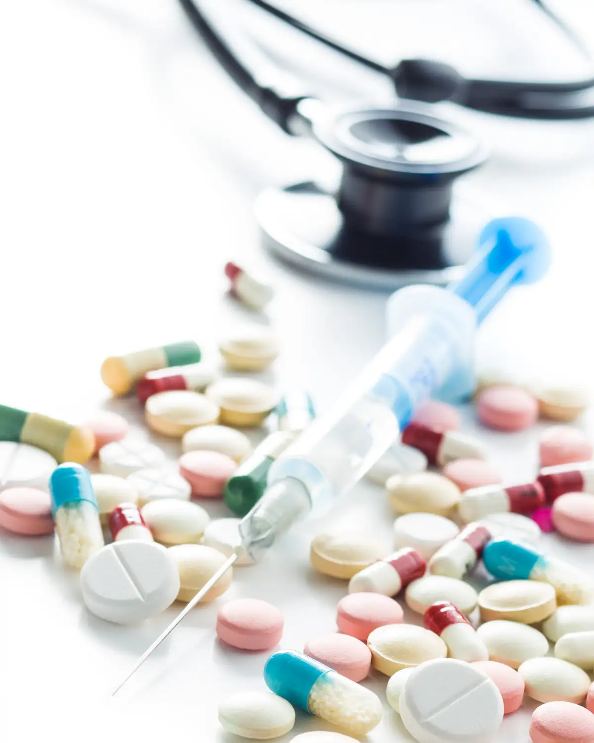 A pile of pills and a syringe on top of the table.