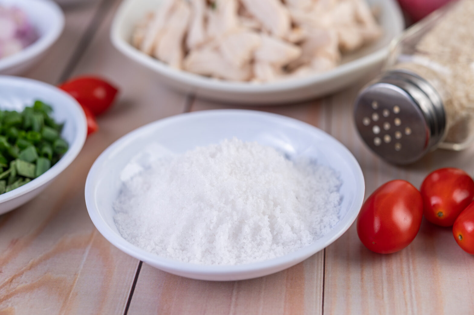 A bowl of flour next to tomatoes and chicken.