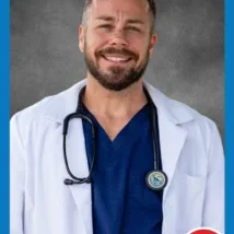 A male doctor wearing a white lab coat and blue scrubs.
