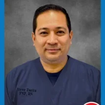 A man in blue scrubs is smiling for the camera.