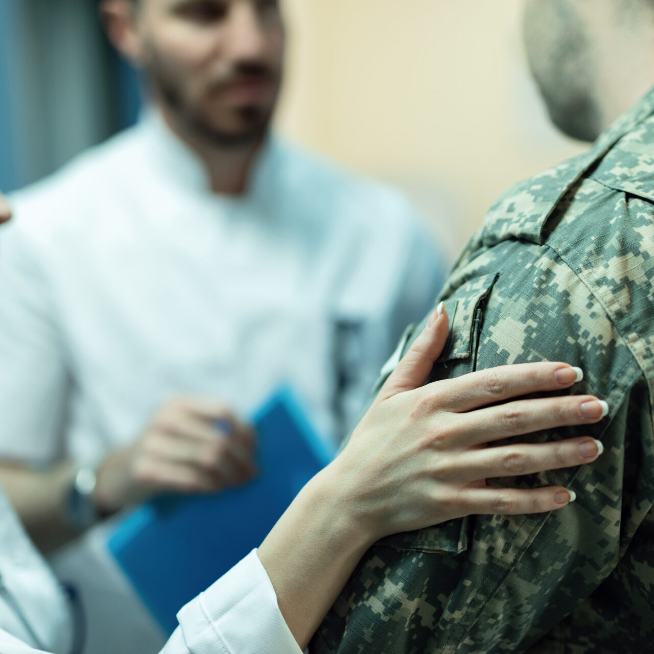 Close up of army soldier being consoled while talking with doctors at clinic.